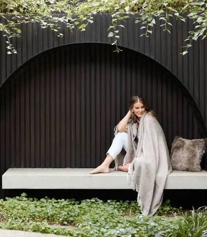 A woman wrapped in a soft throw, seated in a garden setting
